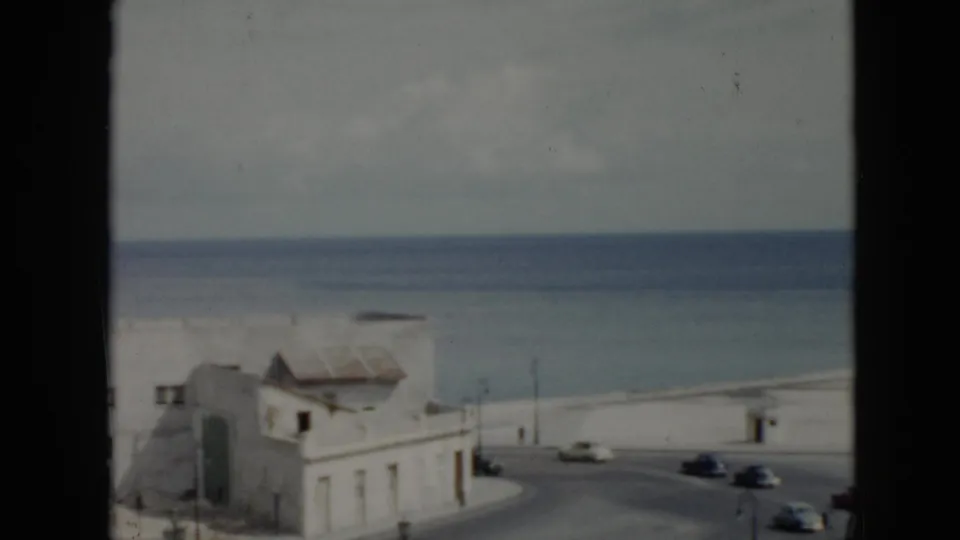 1956 Cuba waterfront buildings and a curving road with mid-century cars, seen in soft color 8mm footage with the sea beyond.