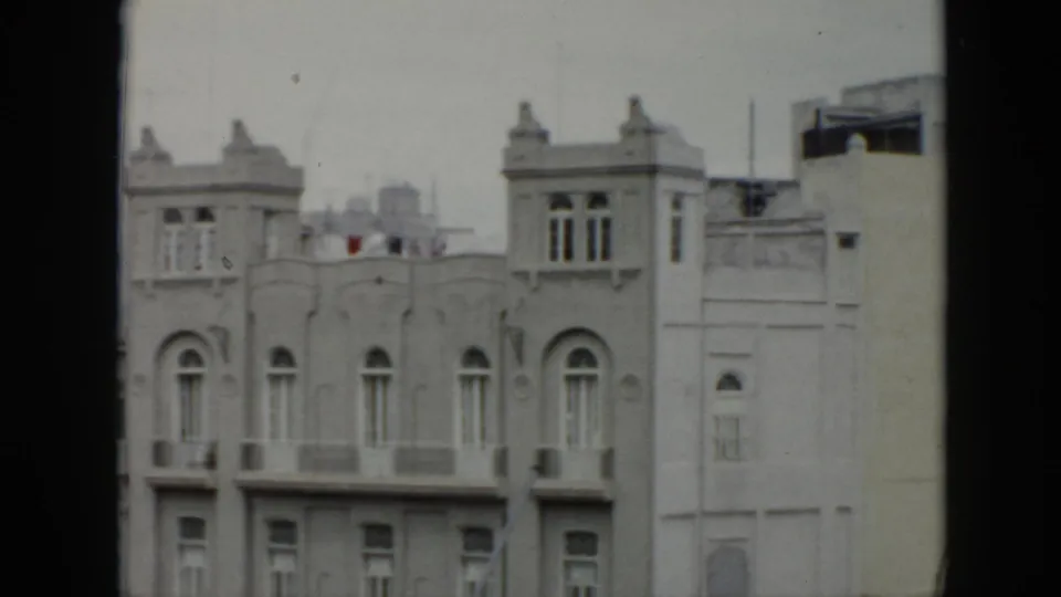 1956 Cuba footage frames an ornate pale urban facade with arched windows, balconies and rooftop architectural details.