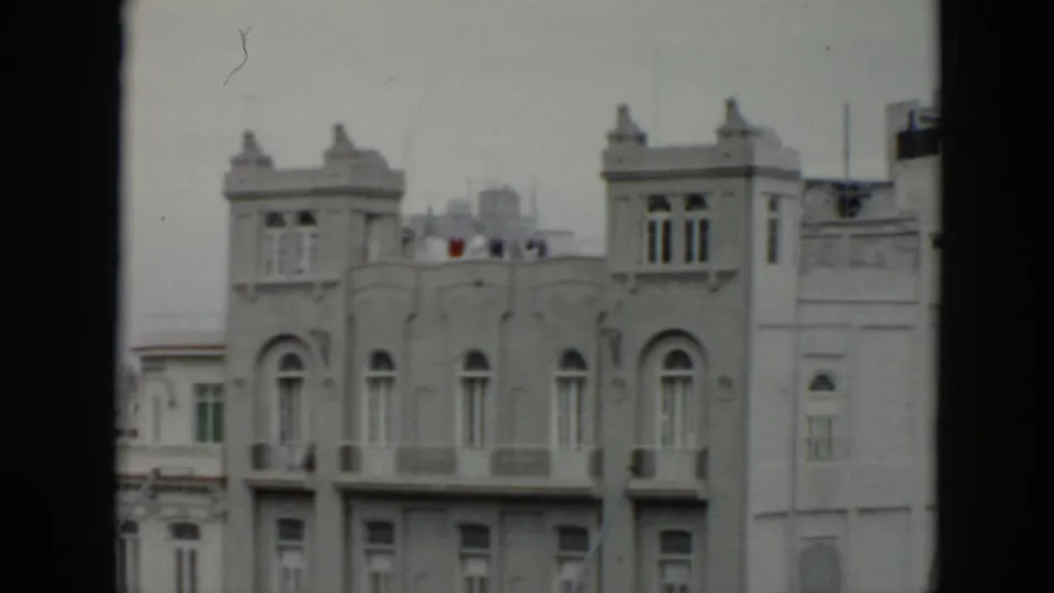 1956 Cuba home-movie frame shows a pale ornate building facade with arched windows, balconies and distant rooftop forms.