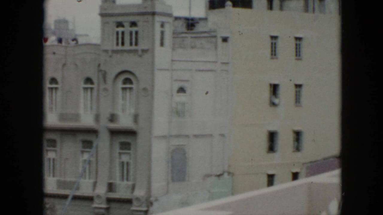 1956 Cuba balcony-view frame with ornate windows on one facade and a plainer neighboring wall with small rectangular windows.