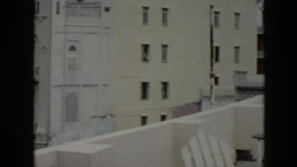 1956 Cuba terrace view with a pale building wall beyond a balcony parapet and a white slatted chair in the foreground.