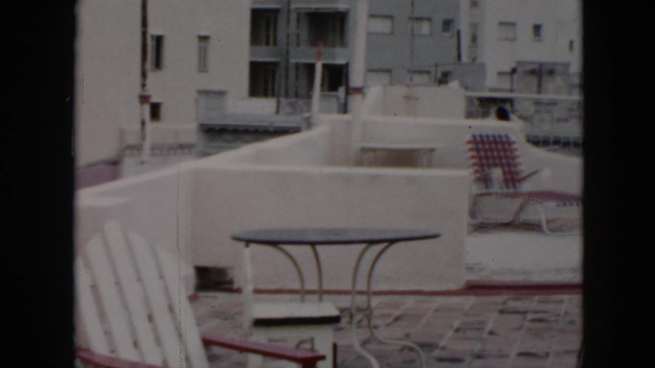 Rooftop patio with a metal table, white chairs, and a patterned lounge chair.