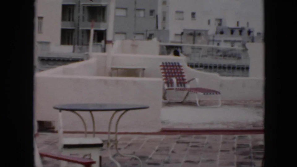 1956 Cuba home-movie frame of a rooftop patio with furniture and neighboring buildings under soft daylight.