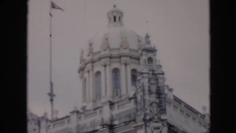 1956 Cuba frame showing an ornate domed building with sculptural details and a Cuban flag on a tall pole.
