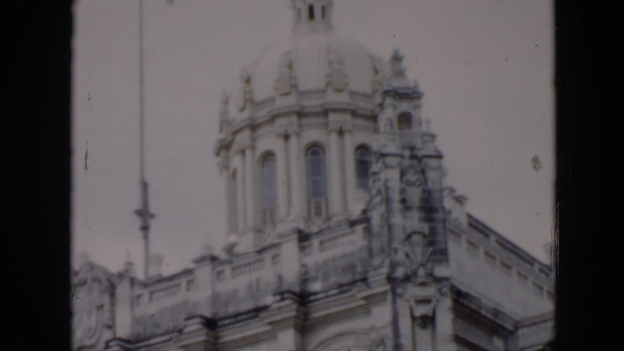1956 Cuba 8mm frame showing the upper facade of an ornate stone building with a dome, carved trim, and arched architectural details.