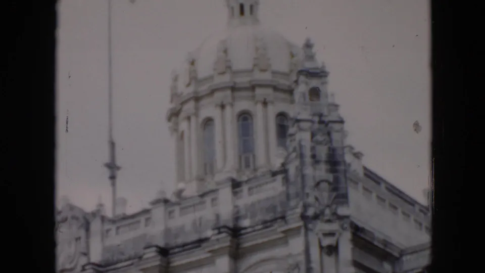 1956 Cuba 8mm frame showing the upper facade of an ornate stone building with a dome, carved trim, and arched architectural details.