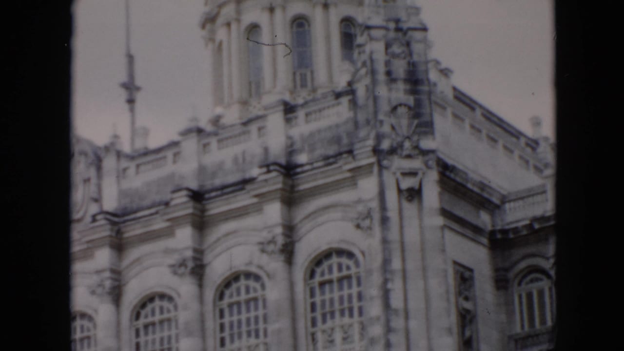 1956 Cuba 8mm frame of an ornate stone facade with tall arched windows, decorative columns, balcony trim, and the base of a dome.