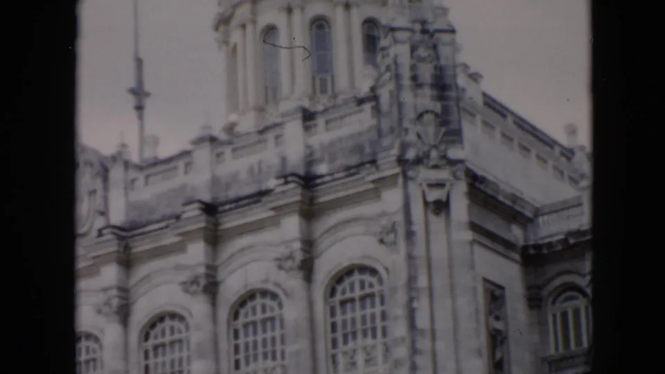 1956 Cuba 8mm frame of an ornate stone facade with tall arched windows, decorative columns, balcony trim, and the base of a dome.