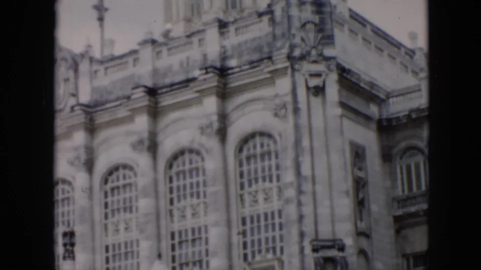 1956 Cuba 8mm frame showing a closer section of the ornate stone building, including arched windows, balcony railing, and carved vertical ornament.