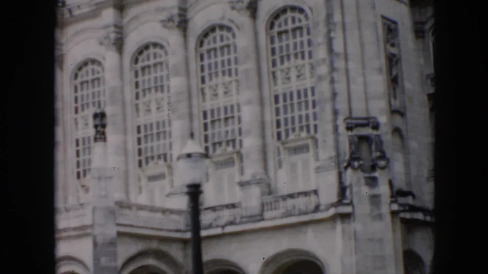 1956 Cuba home-movie frame of an ornate historic facade with arched windows, masonry details, and a streetlamp in the foreground.