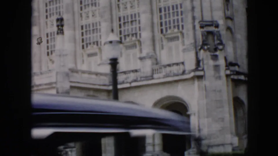 A 1956 Cuba driving shot frames the historic building through dark car silhouettes, with tall windows and a passing roofline across the view.
