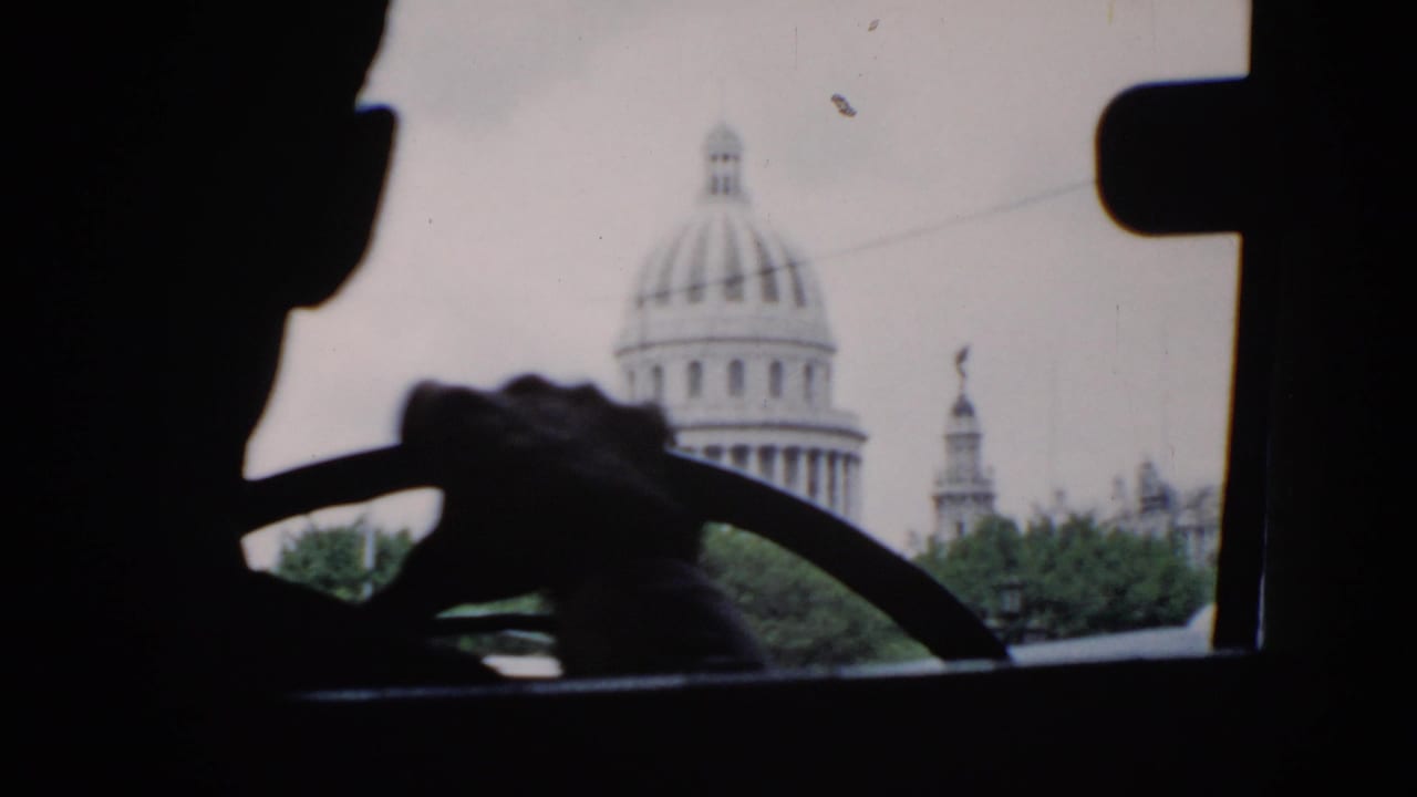 Driver silhouette and steering wheel with a domed capitol-style building visible through the windshield.
