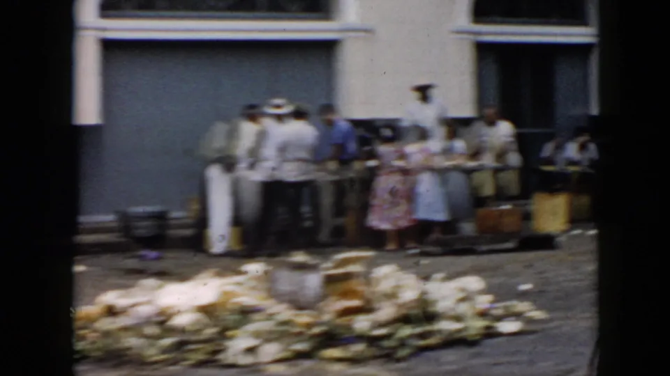 1956 Cuba street scene with pedestrians gathered near curbside fruit stands, produce displays, and scattered debris in the foreground.
