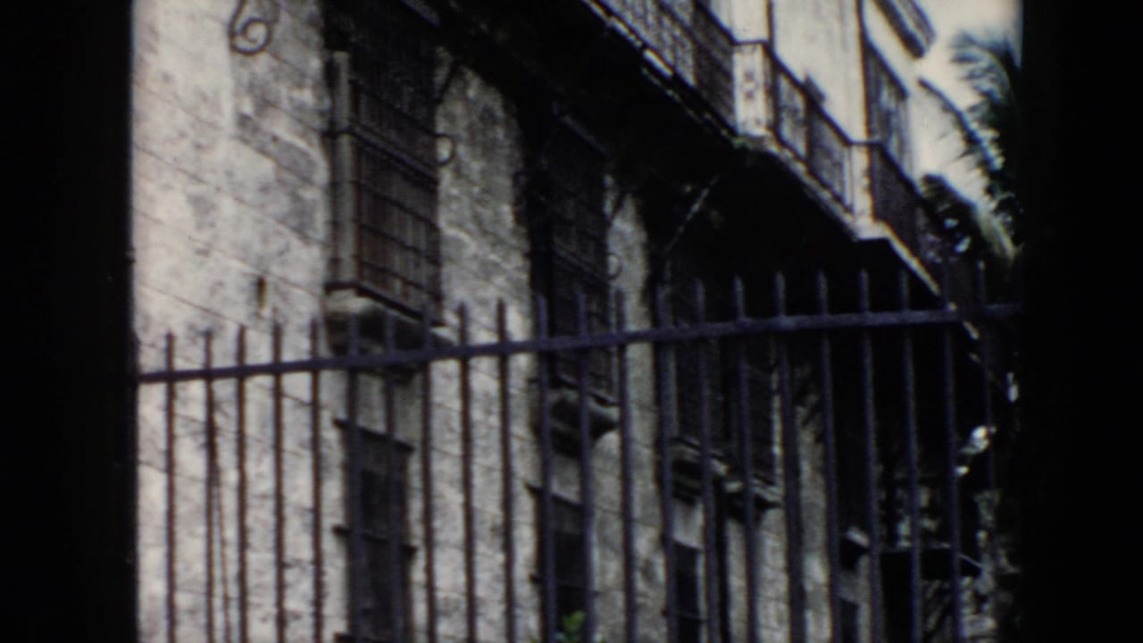 1956 Cuba 8mm frame showing a worn stone facade behind an iron gate, with barred windows and balcony details visible.