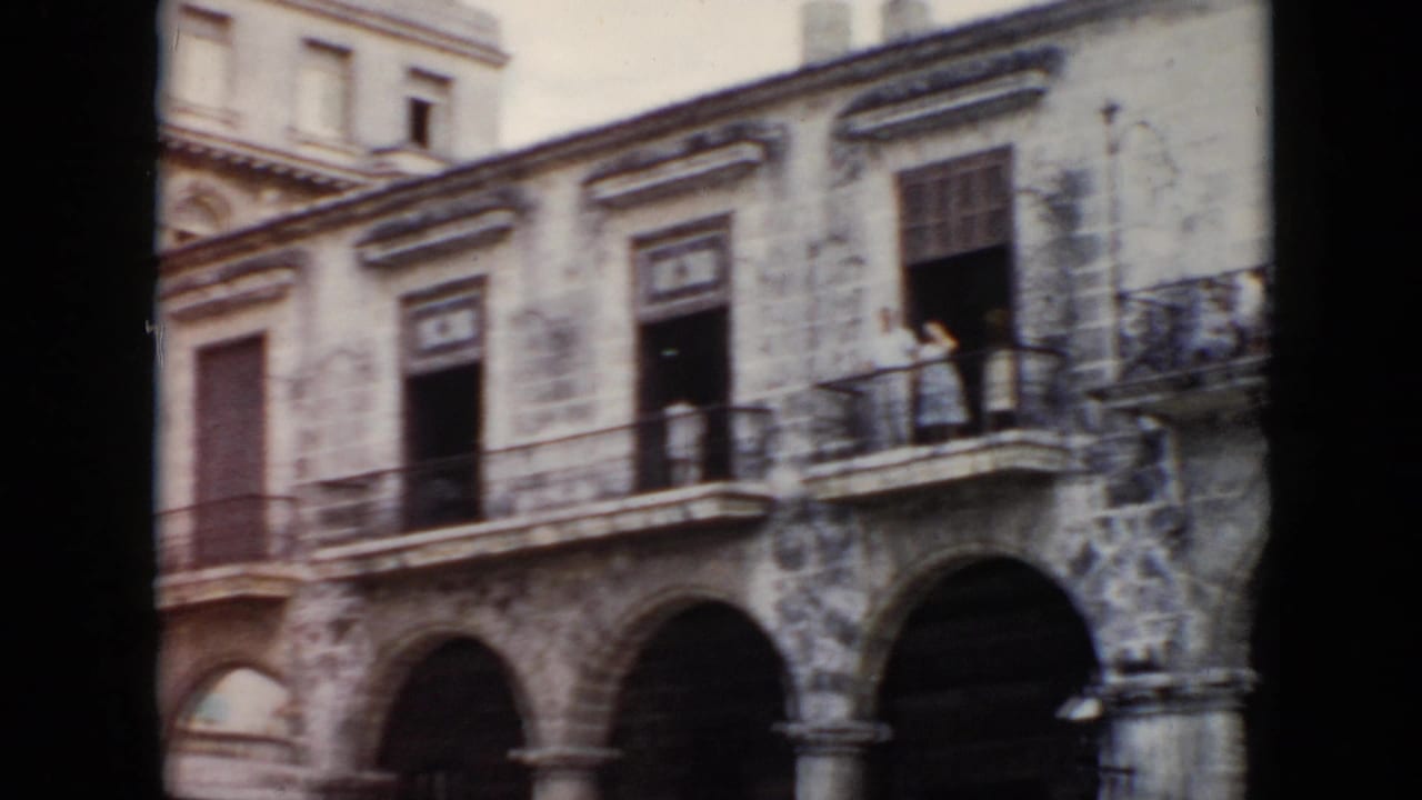 1956 Cuba home-movie frame showing a colonial-style building with stone arches, balconies, and a small figure visible near an upper railing.