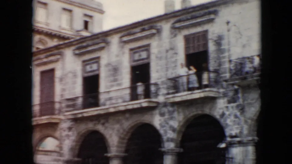 1956 Cuba home-movie frame showing a colonial-style building with stone arches, balconies, and a small figure visible near an upper railing.