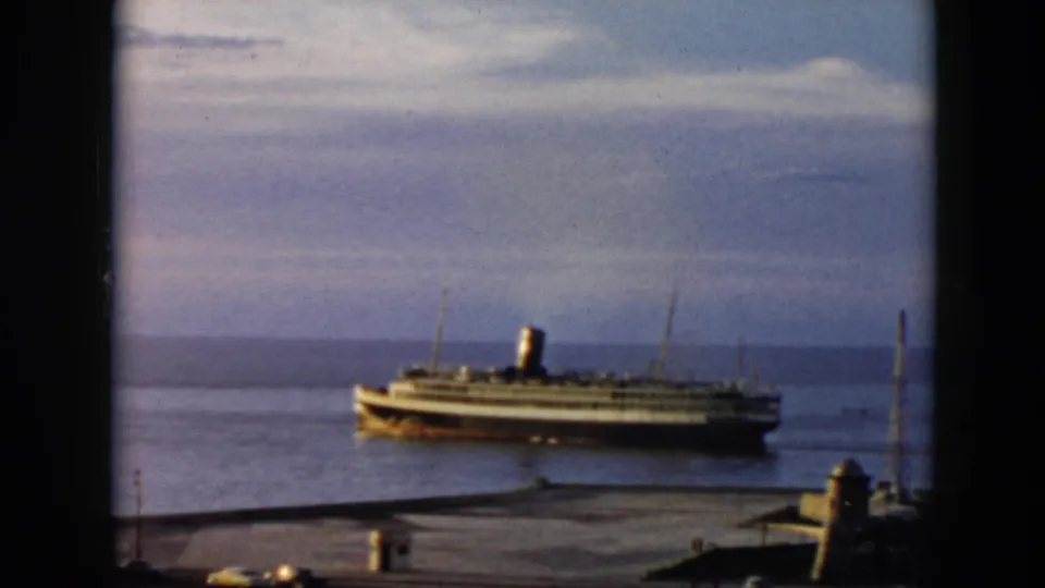 Elevated 1956 Cuba harbor shot with a passenger steamship crossing calm water under a cloudy sky.