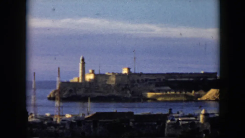 1956 Cuba home-movie frame of a lighthouse on a rocky coastal structure, with harbor details and a dark window frame in view.
