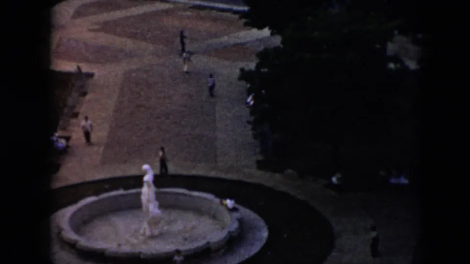 1956 Cuba home-movie frame showing a circular fountain and statue below an elevated viewpoint, with pedestrians spread across the plaza.