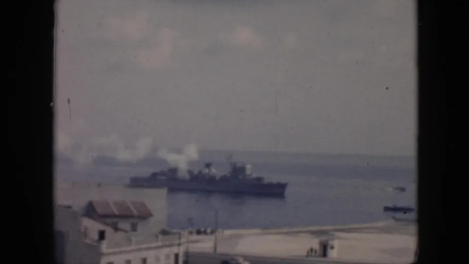 A large vessel with white smoke from its stacks crosses a Cuba harbor, seen from an elevated shoreline viewpoint.