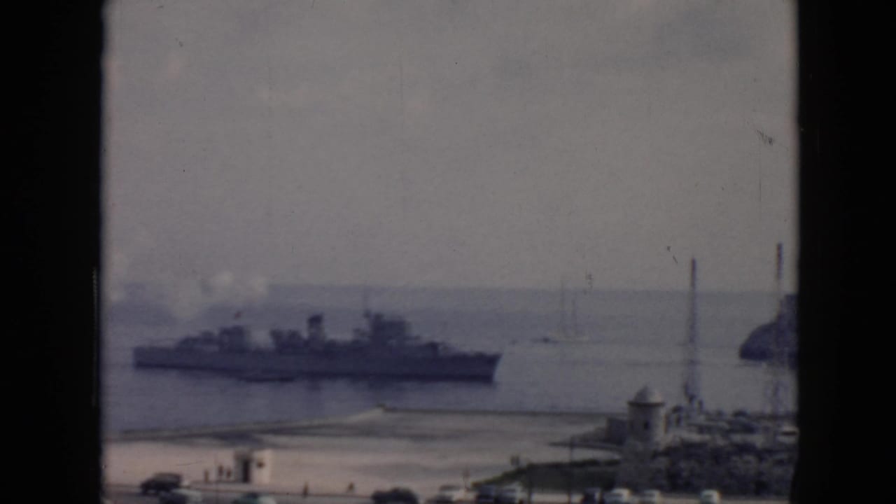 1956 Cuba harbor view with a large warship-like vessel, smoke, small boats, and coastal structures seen from above.