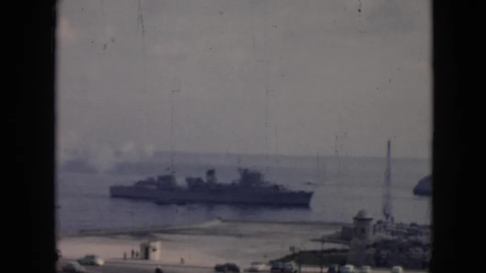 1956 Cuba harbor footage frame with a large naval-style ship, soft smoke, foreground buildings, and tall mast-like structures.