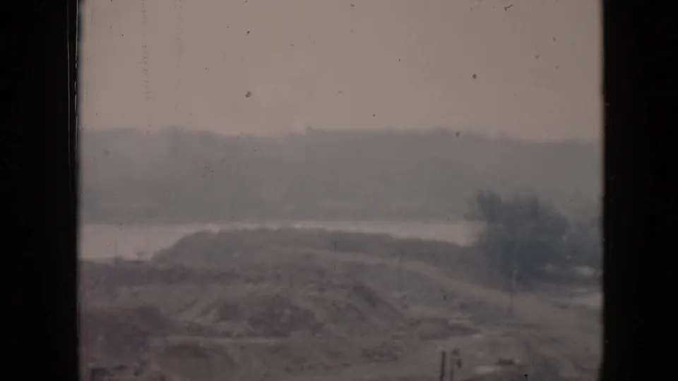1956 Cuba home-movie frame of a low coastal hill or industrial knoll beside water under hazy light.