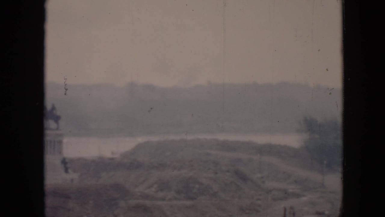 1956 Cuba 8mm frame showing a distant equestrian statue on a pedestal beside water and hills, viewed through a dark window frame.