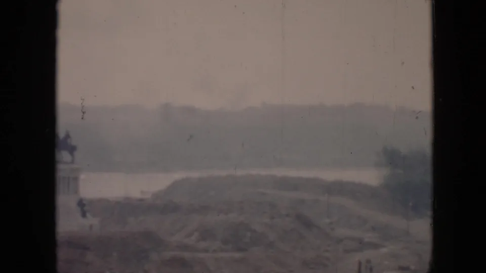 1956 Cuba 8mm frame showing a distant equestrian statue on a pedestal beside water and hills, viewed through a dark window frame.