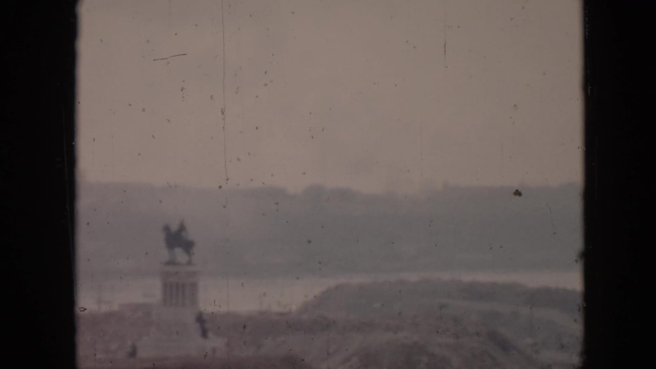 1956 Cuba home-movie frame looking from a balcony toward a hazy coastal scene with a distant statue-like monument and water beyond.
