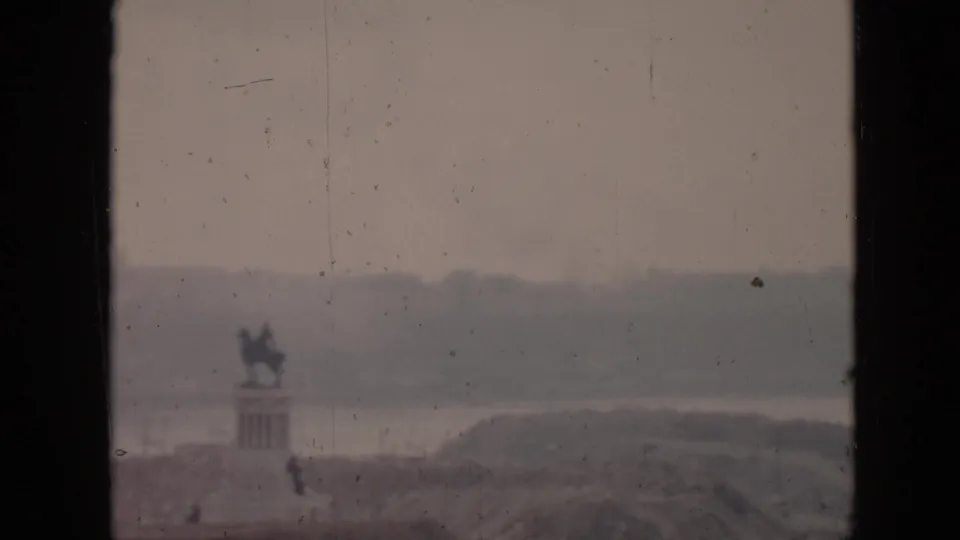 1956 Cuba home-movie frame looking from a balcony toward a hazy coastal scene with a distant statue-like monument and water beyond.