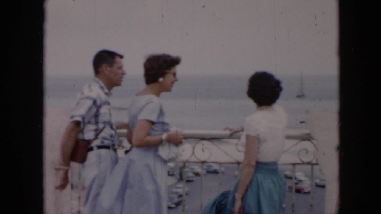 In 1956 Cuba home-movie footage, a man and two women stand by a decorative railing overlooking a coastal harbor.