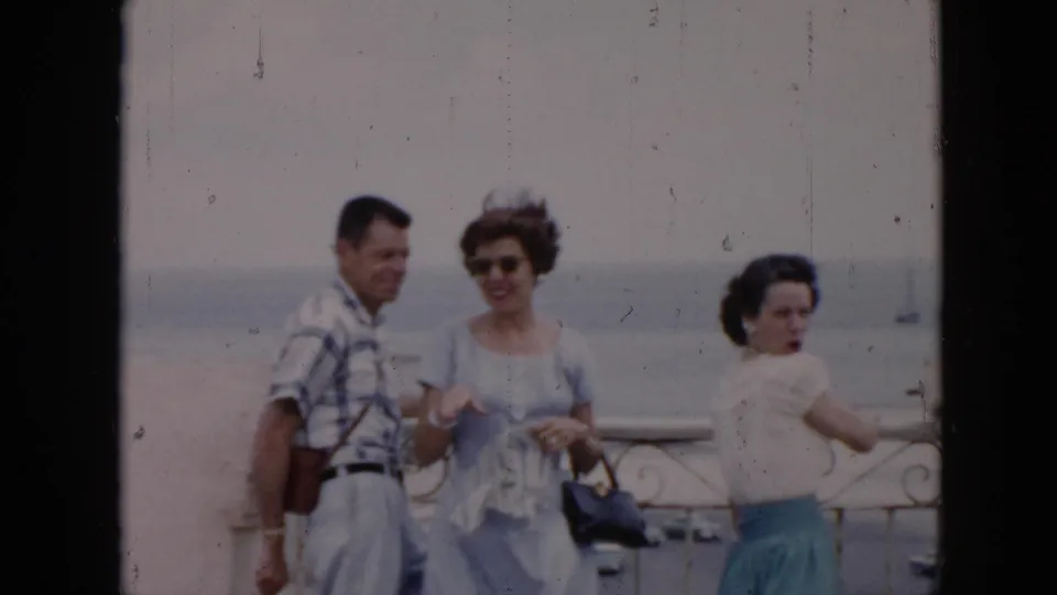 The adults shift position on the balcony, with one woman smiling toward the camera and the harbor still visible behind them.