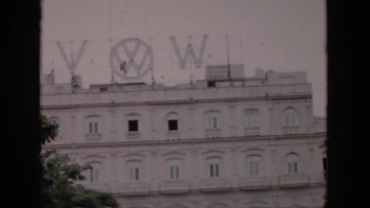 1956 Cuba frame with the Volkswagen logo and letters on a rooftop structure above a pale building with repeated arched windows.