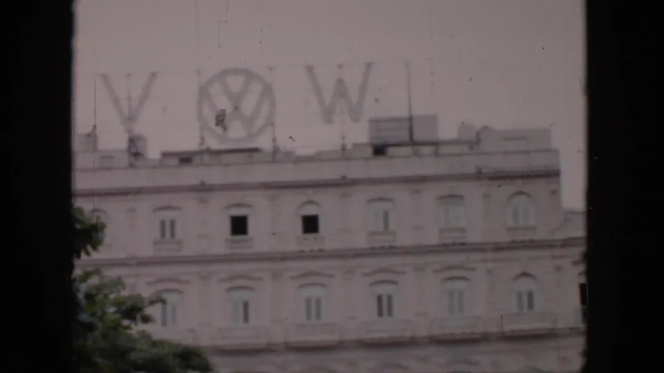 1956 Cuba frame with the Volkswagen logo and letters on a rooftop structure above a pale building with repeated arched windows.