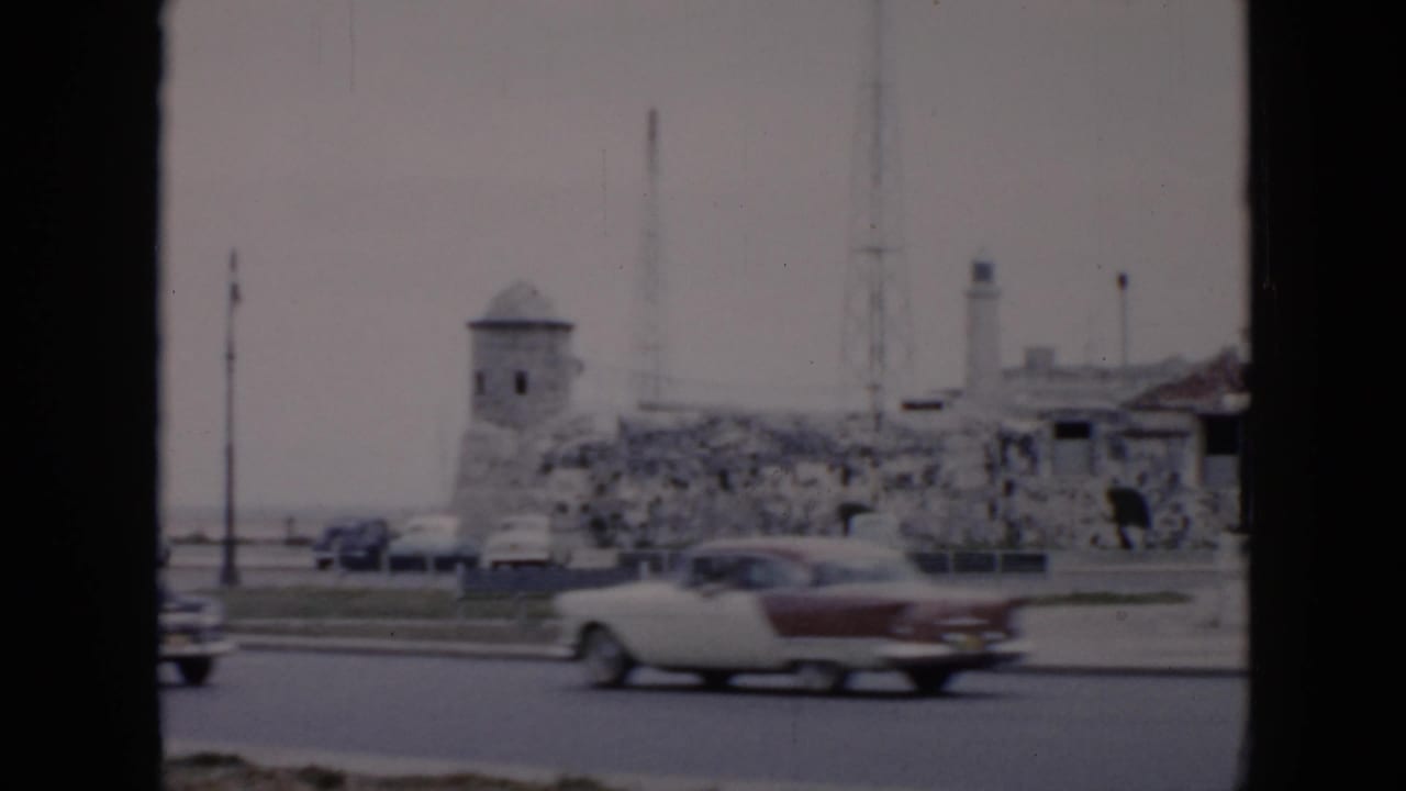 Cars pass a roadway beside stone fortifications and a small tower.