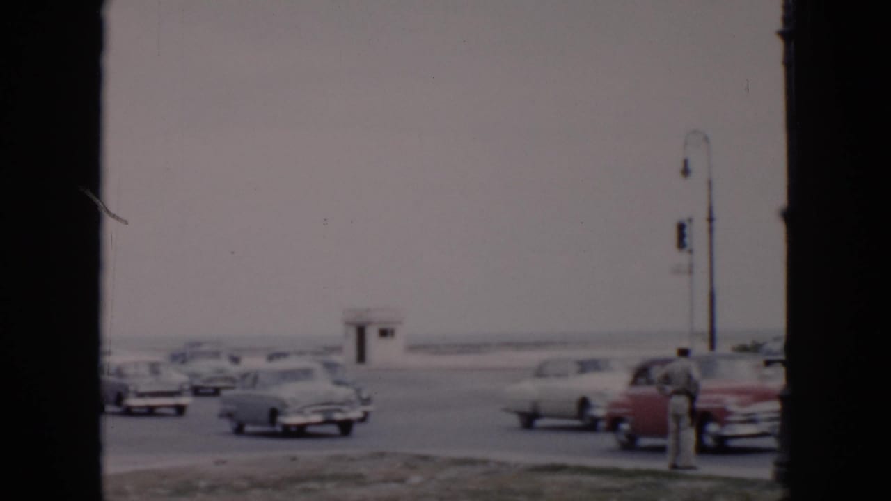 Traffic officer beside classic cars at a broad intersection with a small guardhouse in the background.