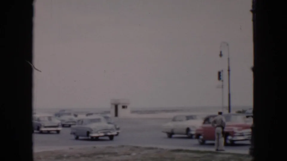 Mid-1950s Cuba intersection with a uniformed traffic officer, classic cars, street lamps, and a small white guardhouse beyond the roadway.