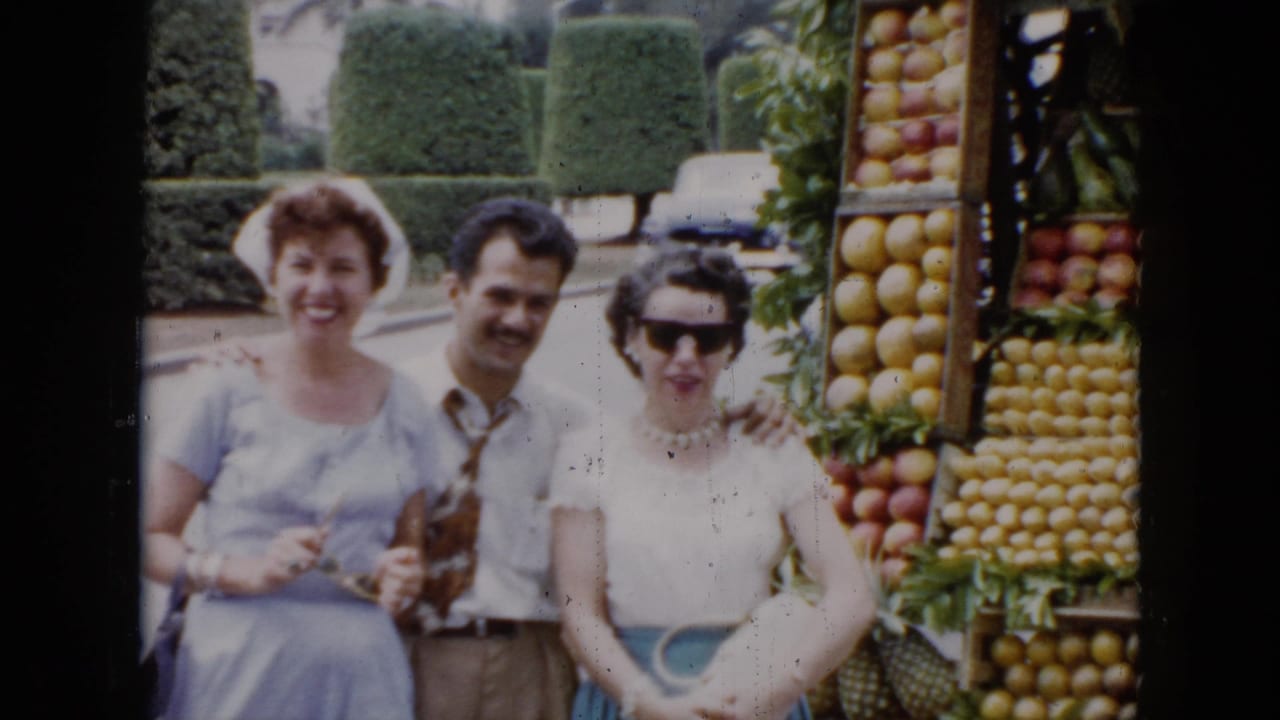 In supplied 1956 Cuba footage, two women and a man pose next to a tiered fruit stand filled with produce.