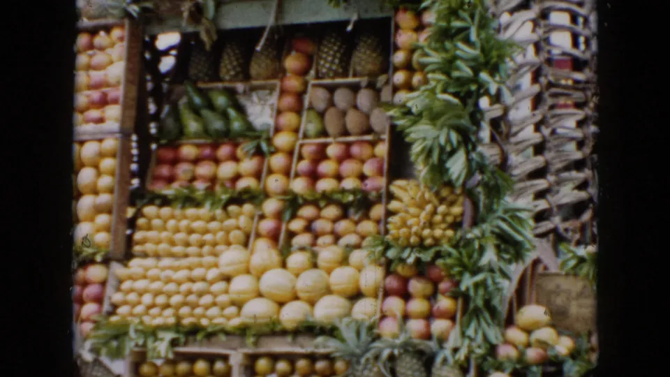 The final 1956 Cuba frame focuses on the fruit stand, showing stacked citrus, apples, melons, pineapples, and bananas.