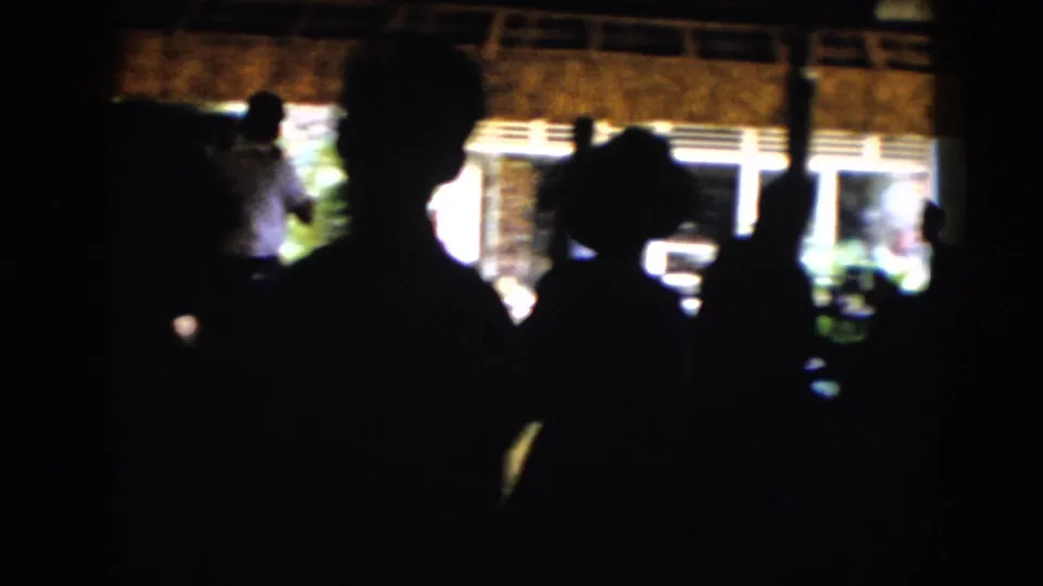 Silhouetted figures stand near bright windows in a dim interior, including one raised arm shape at the right.