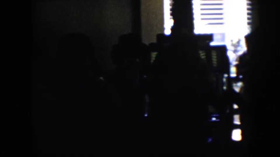 Silhouetted people gather in a dim Cuba party interior, with bright shuttered window light outlining the group.