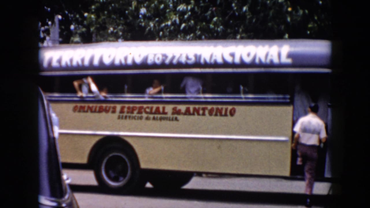 1956 Cuba frame showing the side of a cream omnibus marked with large lettering as passengers wave from open windows.