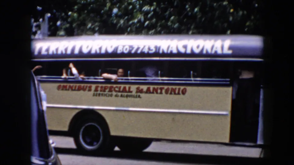 1956 Cuba home-movie frame with a close side view of the cream omnibus, visible painted lettering, and passengers at the windows.