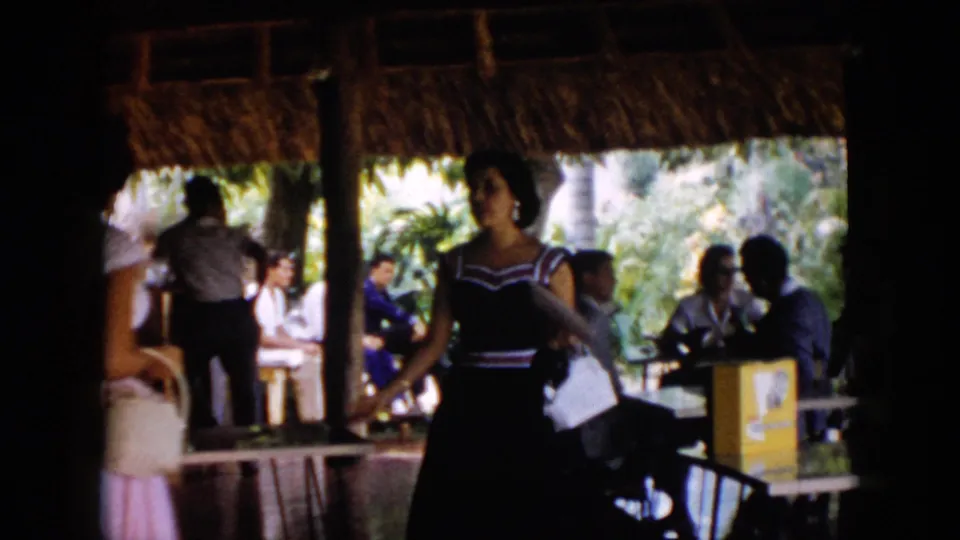 1956 Cuba resort pavilion scene with a woman holding a light handbag near seated guests and dining tables.