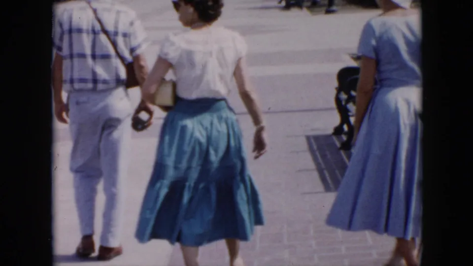 In the Cuba 1956 clip, two women in blue-toned mid-century clothing and a man in light trousers walk away near plaza benches.