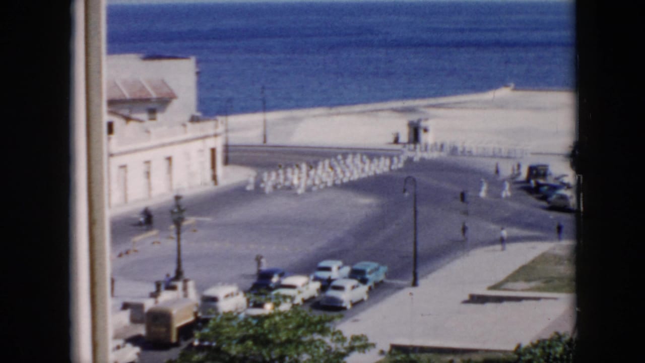 Uniformed personnel march in formation along a broad waterfront road beside the sea.