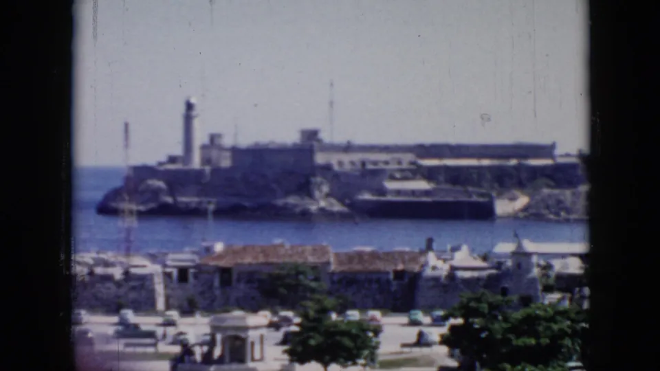 1950s Cuba home-movie view across water toward a fort-like structure with a tall tower, seen above low city buildings.