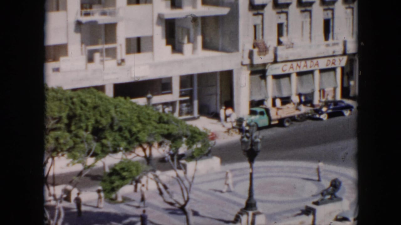 1950s Cuba street scene with pedestrians, vintage cars, a circular plaza, trees, and a Canada Dry storefront sign.