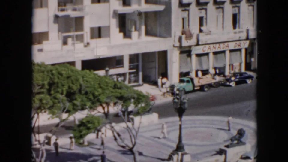 1950s Cuba street scene with pedestrians, vintage cars, a circular plaza, trees, and a Canada Dry storefront sign.